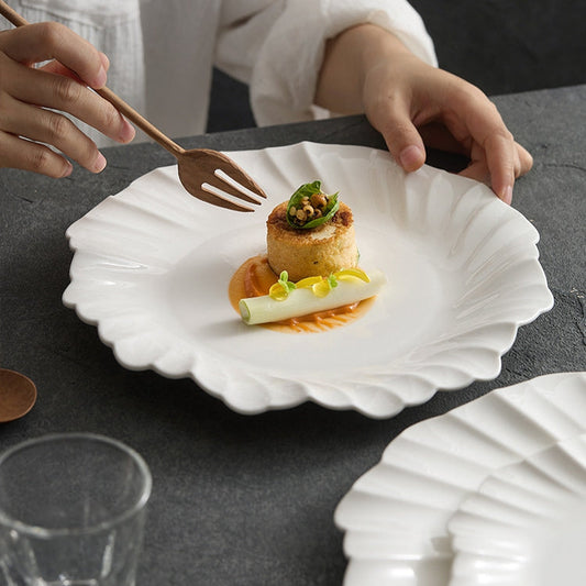 Delicate dish on a white shell-shaped plate with a person holding a fork, set against a dark surface.