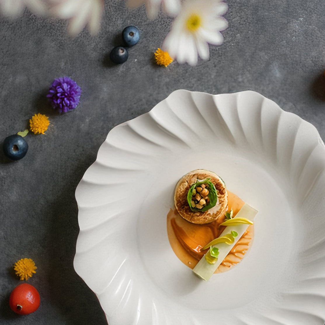 Delicate dessert on a white plate with flowers and fruits on a dark surface