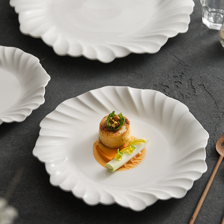 White scalloped plates with a small dish of food on a dark surface