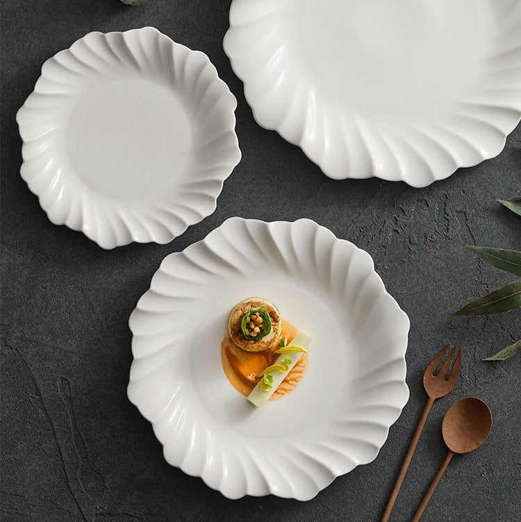 Set of white ceramic plates on a dark surface with a small dish of food and wooden utensils.