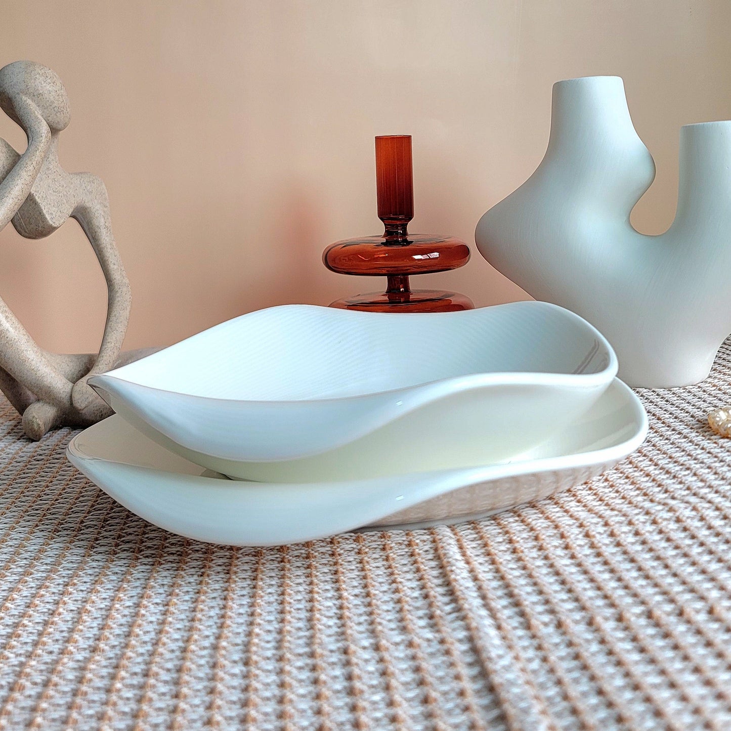 Decorative items including a white bowl, a red candle holder, and a white vase on a textured surface.