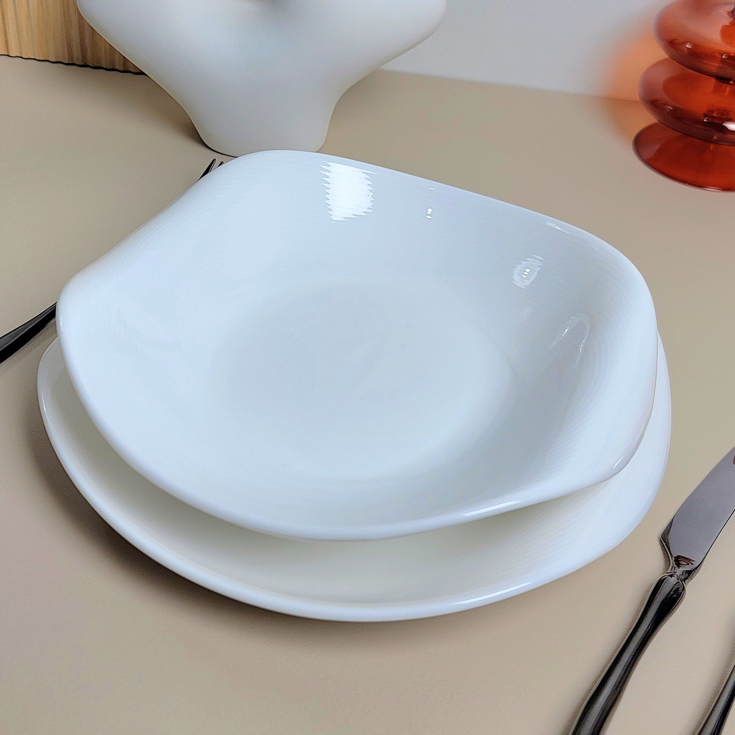 White ceramic bowl on a beige surface with a white vase and red object in the background.