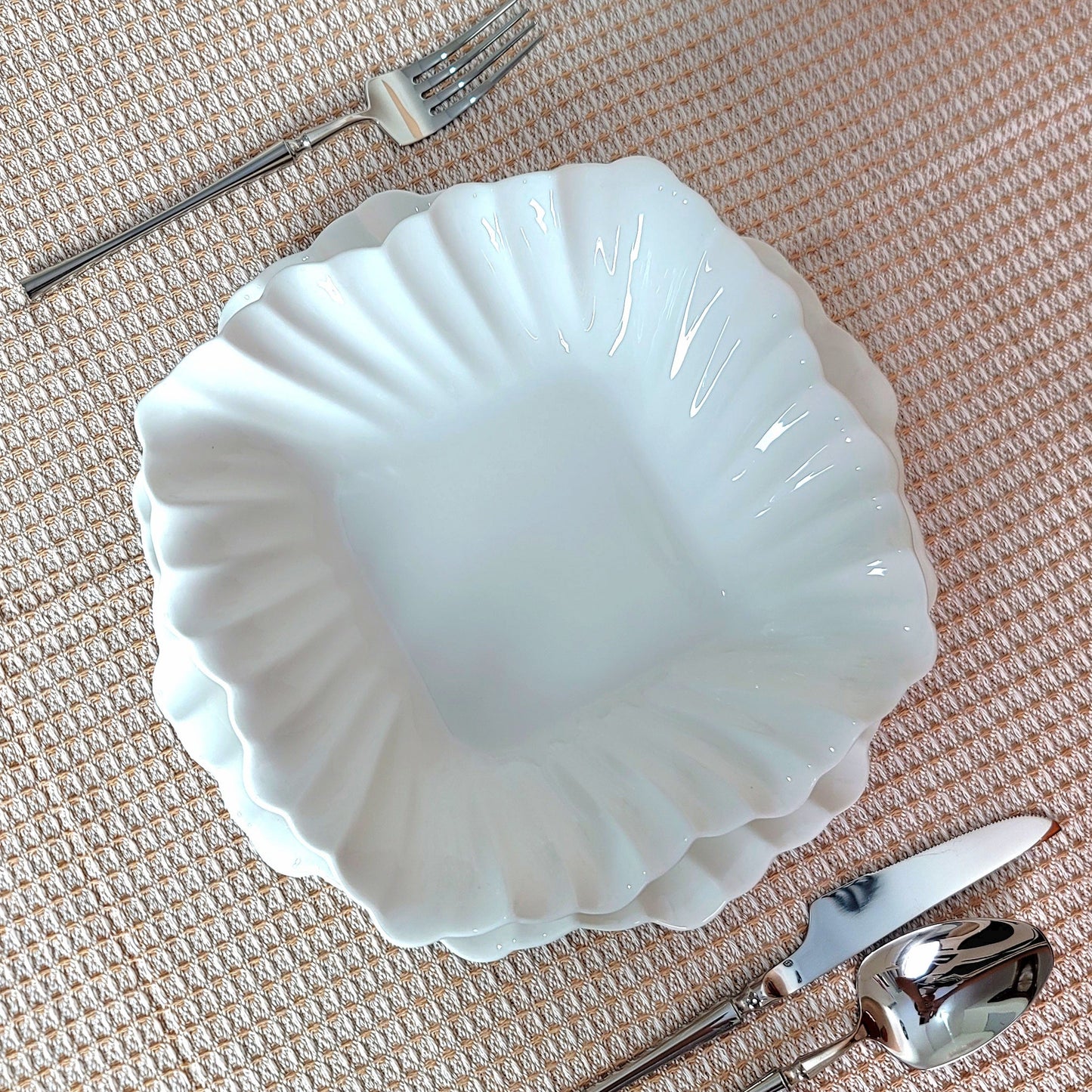 White ceramic shell-shaped bowl with silverware on a textured surface