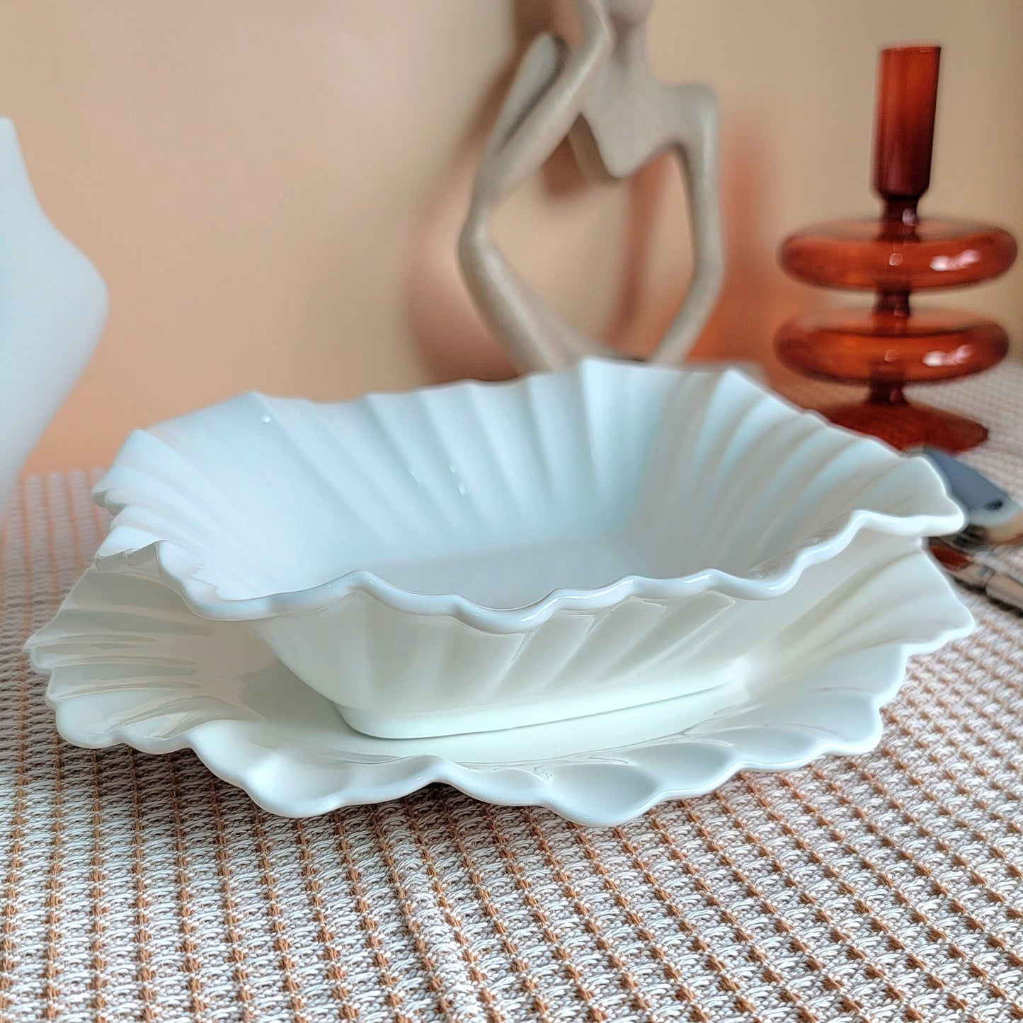 White scalloped-edge bowl on a textured surface with decorative items in the background