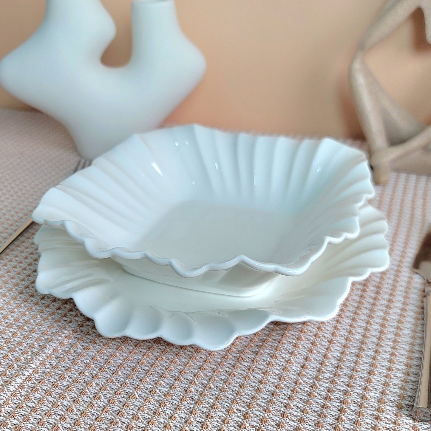 White ceramic shell-shaped dishes on a textured surface with a beige background