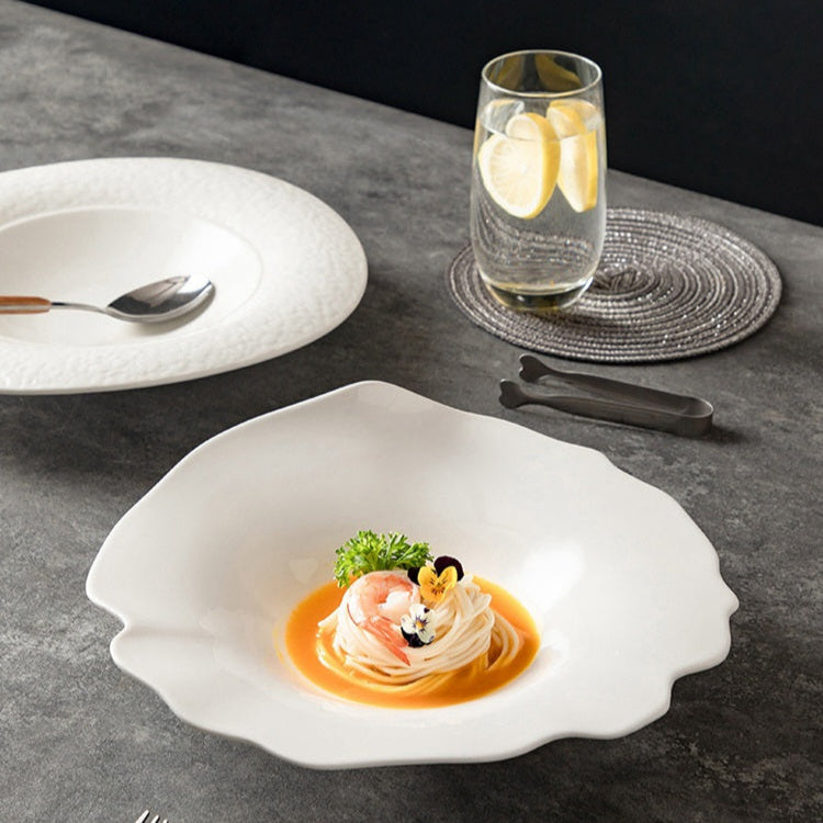 Delicate dish with shrimp and sauce on a white plate, accompanied by a glass of water and lemon slices on a dark surface.