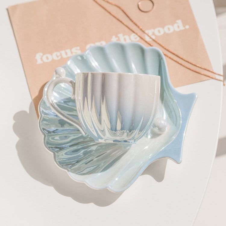 Designed to mimic the graceful curves of a seashell, each piece boasts a delicate iridescent finish that catches the light, evoking the shimmer of ocean pearls. The sculpted handle features a charming pearl-like accent,