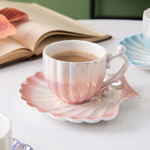 Designed to mimic the graceful curves of a seashell, each piece boasts a delicate iridescent finish that catches the light, evoking the shimmer of ocean pearls. The sculpted handle features a charming pearl-like accent,