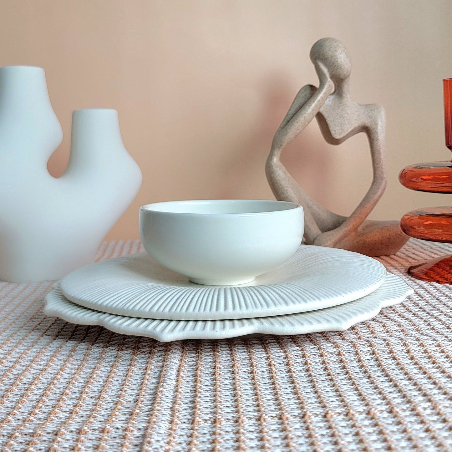 White bowl on a textured tablecloth with decorative vases and a sculpture in the background.