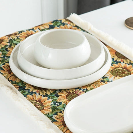 Dinner setup with white bowls, a floral placemat, and gold cutlery on a textured surface.