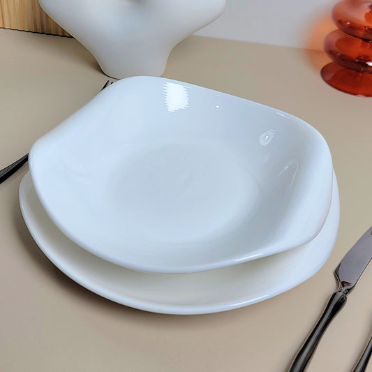 White ceramic bowl on a beige surface with a white vase and red object in the background.