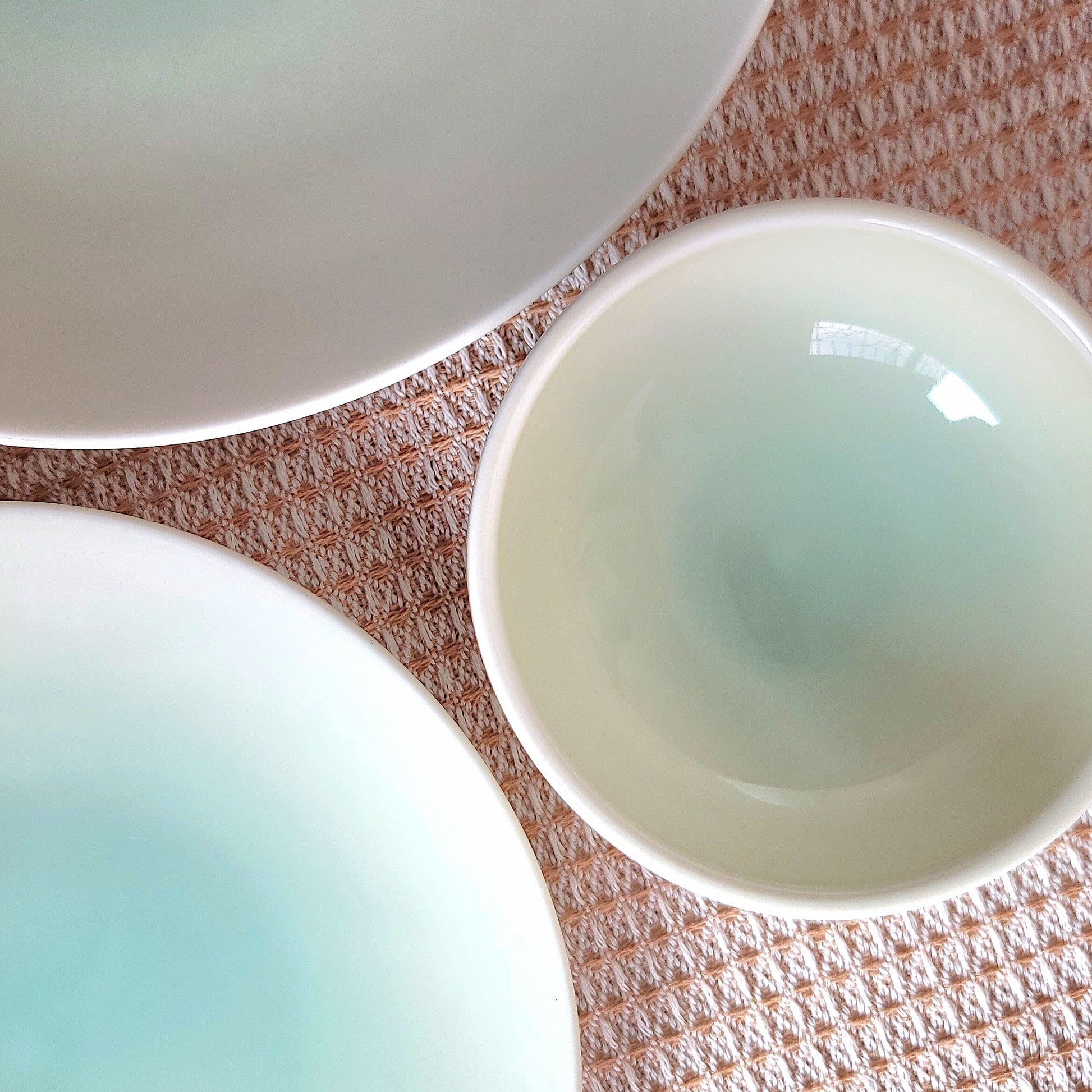 Three jade ceramic bowls on a textured surface