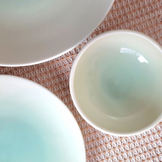 Three jade ceramic bowls on a textured surface