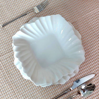 White ceramic shell-shaped bowl with silverware on a textured surface
