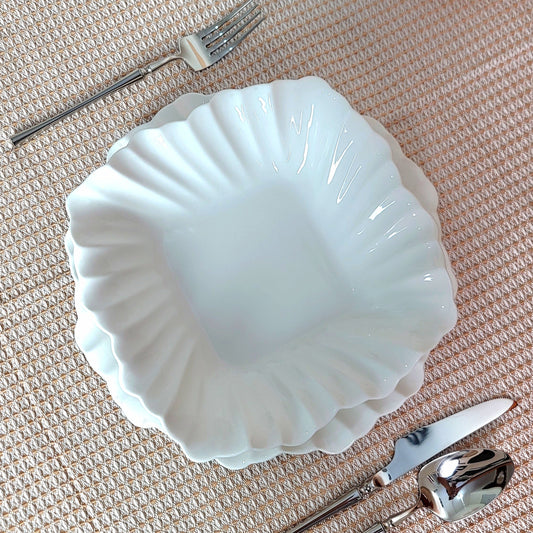 White ceramic shell-shaped bowl with silverware on a textured surface