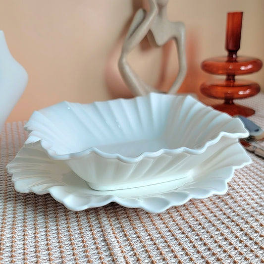White scalloped-edge bowl on a textured surface with decorative items in the background