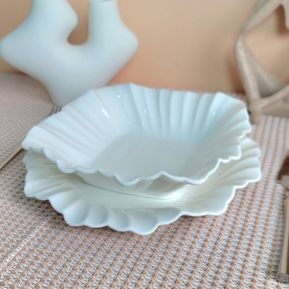 White ceramic shell-shaped dishes on a textured surface with a beige background