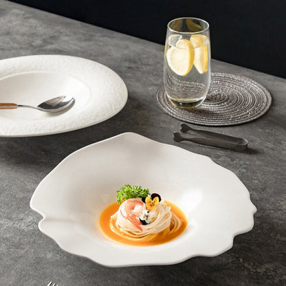 Delicate dish with shrimp and sauce on a white plate, accompanied by a glass of water and lemon slices on a dark surface.