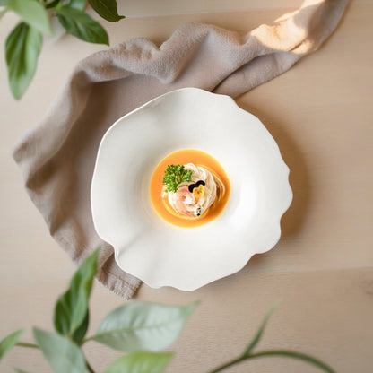 Delicate dish served in a white shell with garnishes, placed on a beige surface with green leaves in the background.