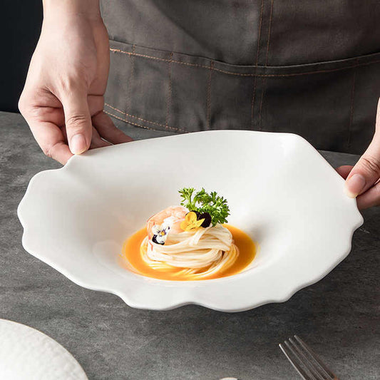 Person holding a white decorative plate with a dish on a gray surface