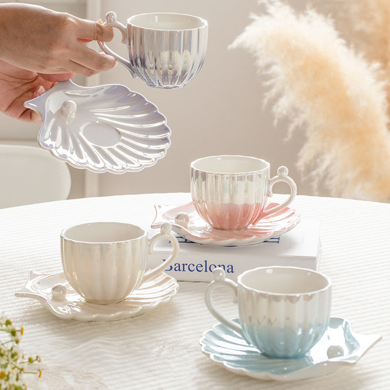 Designed to mimic the graceful curves of a seashell, each piece boasts a delicate iridescent finish that catches the light, evoking the shimmer of ocean pearls. The sculpted handle features a charming pearl-like accent,