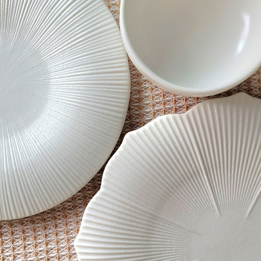 Three white ceramic plates with textured design on a woven surface